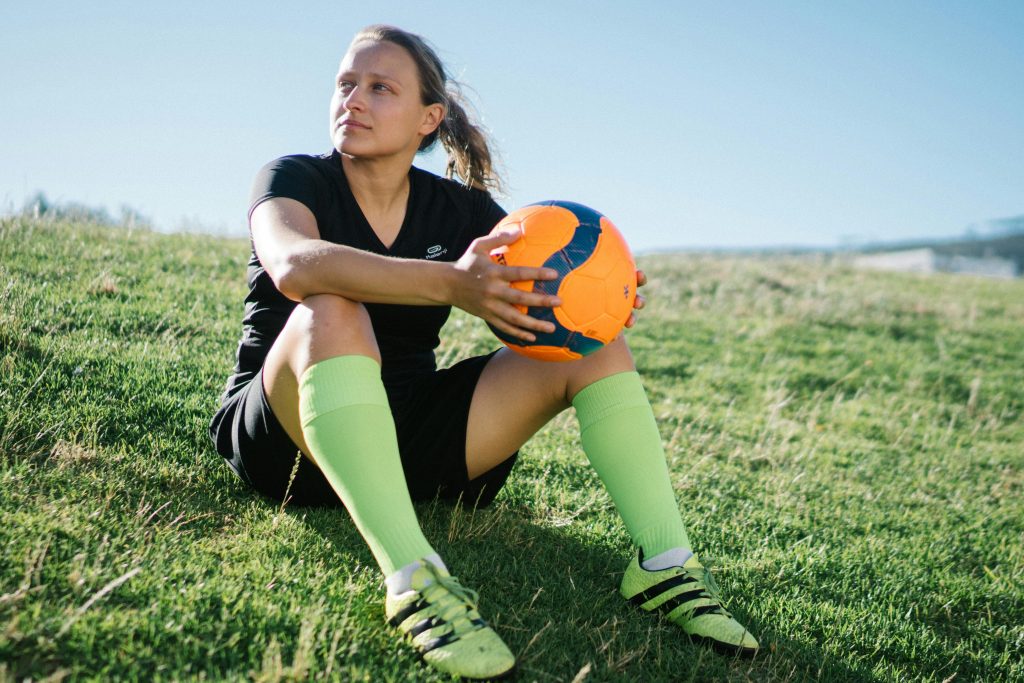 Young female soccer player relaxing with an orange ball on a sunny, grassy field.